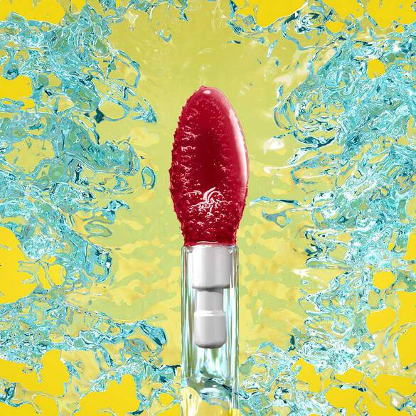 A vibrant red lip balm surrounded by splashes of blue water against a bright yellow background.