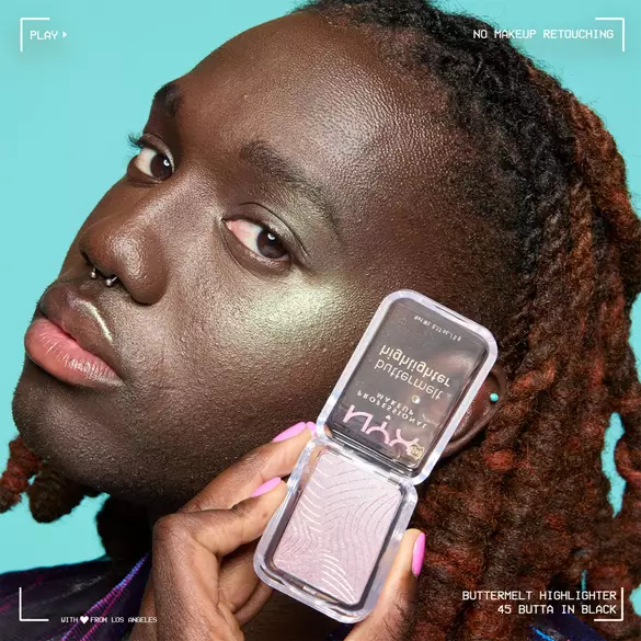 A close-up of a person with dark skin and red-brown hair, holding a highlighter compact against a teal background.