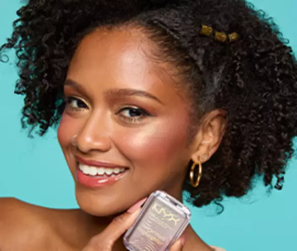 A smiling model with curly hair holds a NYX cosmetics product against a turquoise background, showcasing a vibrant makeup look.